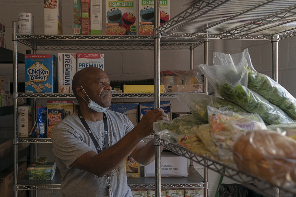 Jumain Lark looks at the street at the Sojourner Truth Ministries food pantry before it opens, in Williamsport, Pennsylvania, on August 3, 2022. Lark works at the food pantry mainly as a cook, which he was hired for through Associates for Training and Development (A4TD). Lark's daughter and two grandchildren live with him; his daughter uses the one car to commute to her job at the nearby federal correctional facility, so Lark typically rides his bicycle 20 minutes to work. Lark provides childcare for his grandchildren in the afternoon before his daughter returns from work.